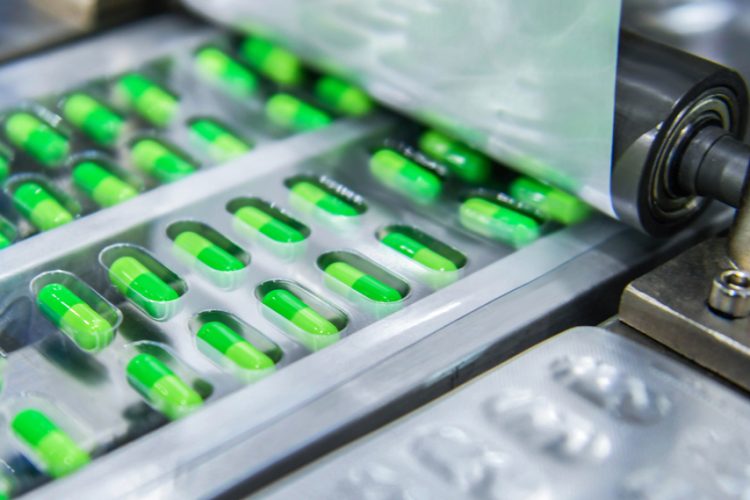 Green capsules being packaged into blister packs - close up of roller applying the lidding foil