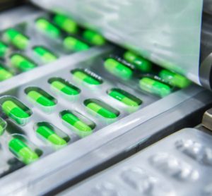 Green capsules being packaged into blister packs - close up of roller applying the lidding foil