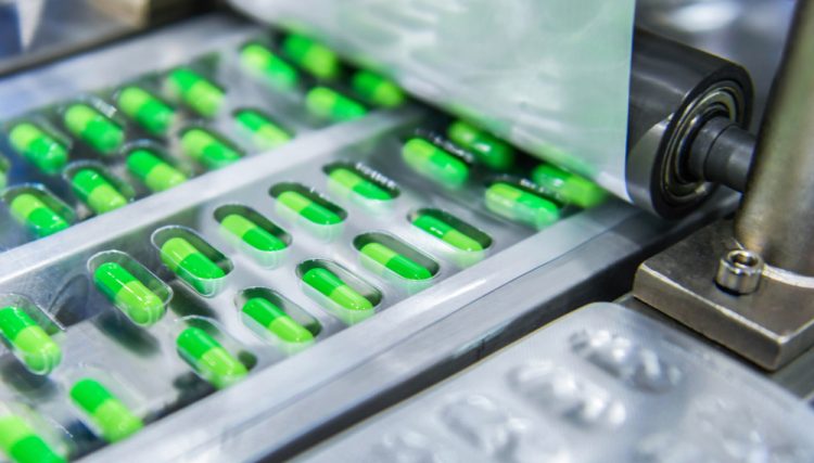 Green capsules being packaged into blister packs - close up of roller applying the lidding foil