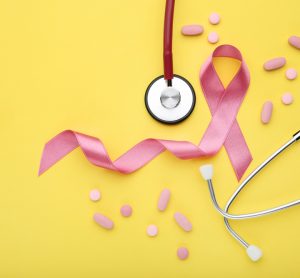 Pink Breast Cancer ribbon, stethoscope and pink pills on a yellow background - idea of breast cancer treatment