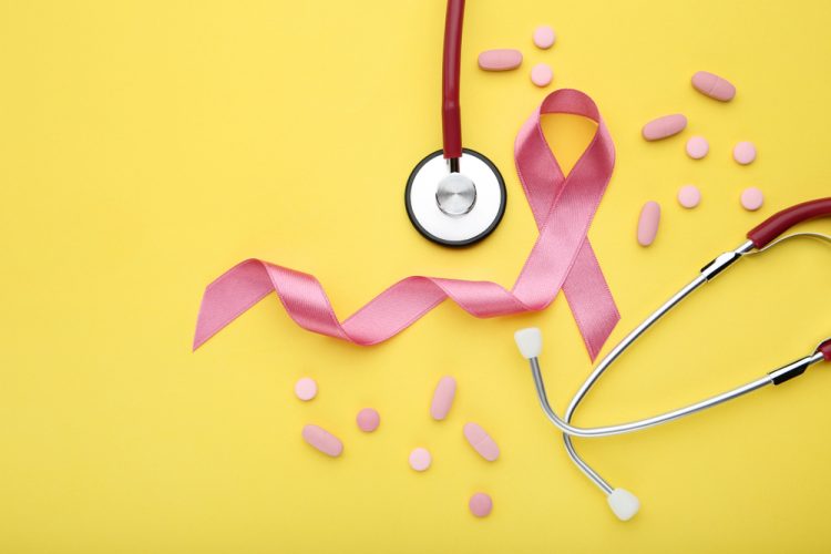 Pink Breast Cancer ribbon, stethoscope and pink pills on a yellow background - idea of breast cancer treatment