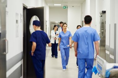 a hospital corridors with numerous doctors in blue scrubs walking along it