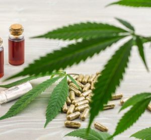 Cannabis leaves on a table next to extracts/oils in bottles and green-grey capsules - idea of cannabis-based medications