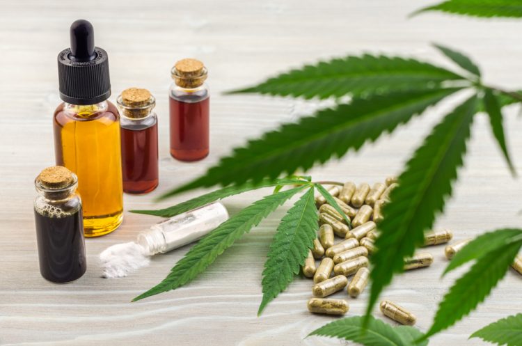 Cannabis leaves on a table next to extracts/oils in bottles and green-grey capsules - idea of cannabis-based medications