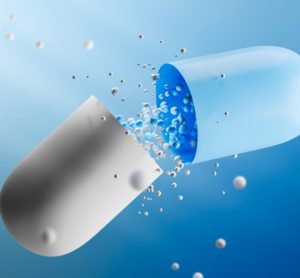 Large open white and blue capsule with medicine leaking from it over a blue background