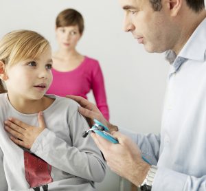 female child with hand over chest - indicating trouble breathing - next to doctor in white room