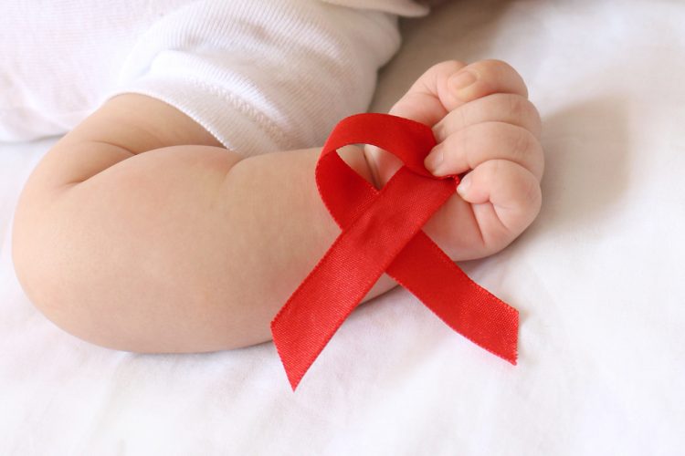 AIDS awareness red ribbon held in the hand of a small baby