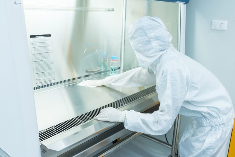 A scientist in sterile coverall gown using alcohol 70% and cleanroom wipes for cleaning Biological safety cabinet(BSC.) in laboratory