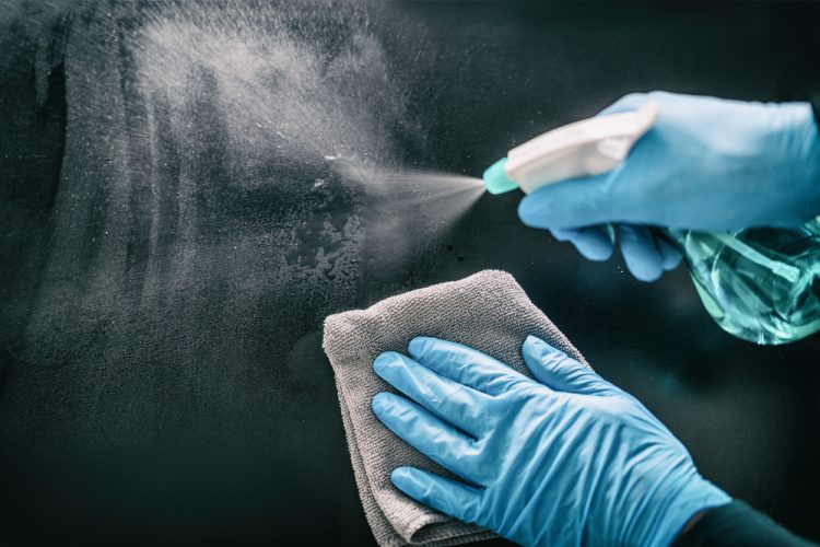 Close up of person's hands spraying and wiping a metal surface - idea of cleaning