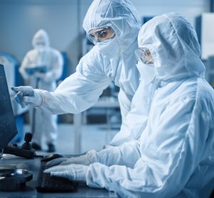 two workers in cleanroom garments looking at a computer in a cleanroom manufacturing facility