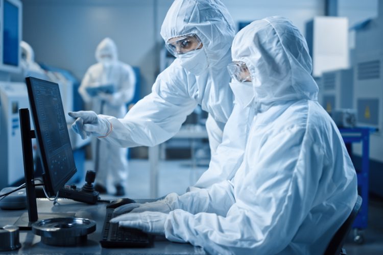two workers in cleanroom garments looking at a computer in a cleanroom manufacturing facility