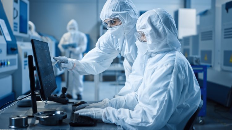 two workers in cleanroom garments looking at a computer in a cleanroom manufacturing facility