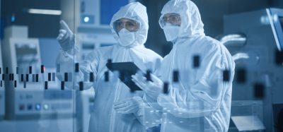 Two people wearing cleanroom garments and gloves looking at a computer tablet in a manufacturing cleanroom facility