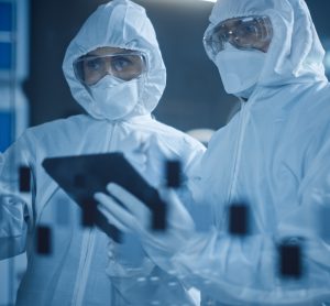 Factory Cleanroom: Engineer and Scientist Wearing Coveralls, Standing in Workshop Talk and Use Tablet Computer, Professionals Develop Technology for Modern CNC Machinery and Electronic Equipment