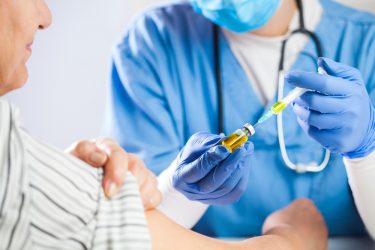 Female doctor drawing a liquid from a vial into a syringe to give to elderly female patient - idea of clinical research/trial