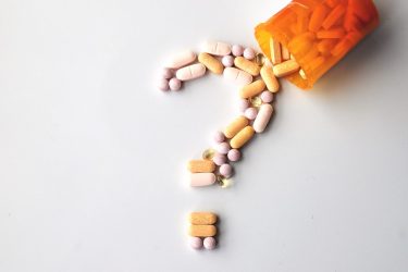 Various shapes and clolours of pills spilling out of an orange prescription bottle and forming the shape of a question mark - idea of drug safety/clinical research
