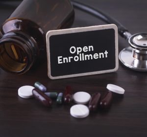 medicine bottle with stethoscope and black and white tables surrounding a sign saying 'open enrollment'