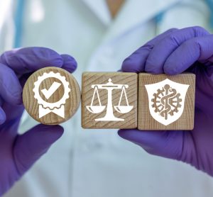 idea of pharmaceutical or clinical trial regulation: close up of a doctors gloved hands holding up three wooden blocks with symbols for regelation or legislation, medicine and approval or certification