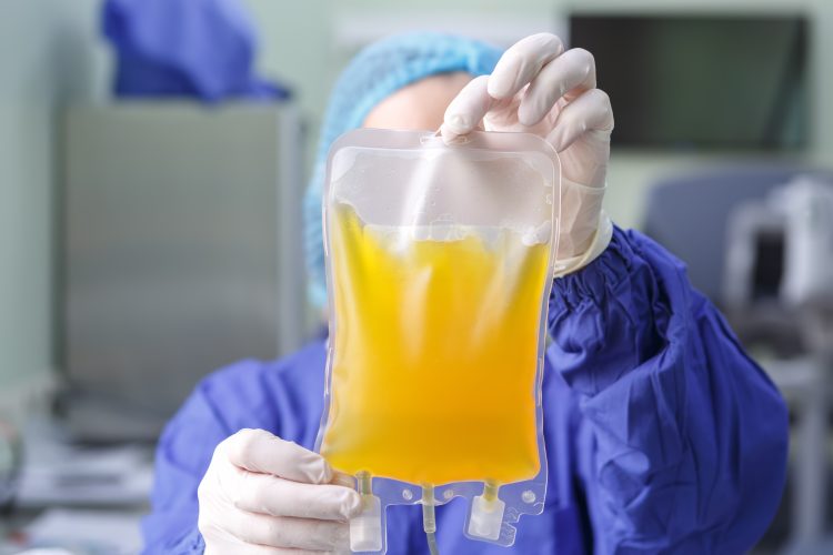 blood plasma in an IV bag held up by doctor wearing PPE