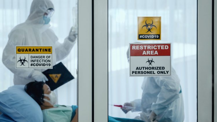 doctors in Personal Protective Equipment (PPE) in the room of a hospitalised COVID-19 patient