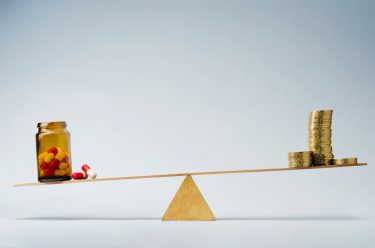 stack of coins and a bottle of pills balancing at either end of a seesaw - idea of budget for/cost of medicines