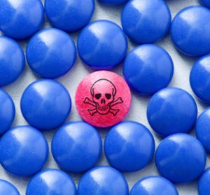 idea of fake or counterfeit pharmaceuticals - one red pill with skull and crossbones on (indicating danger) surrounded by blue ones of the same shape and size