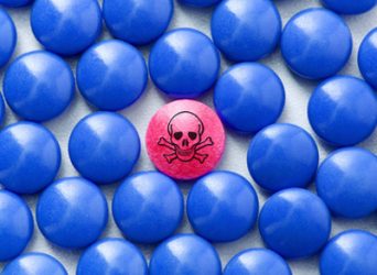 idea of fake or counterfeit pharmaceuticals - one red pill with skull and crossbones on (indicating danger) surrounded by blue ones of the same shape and size