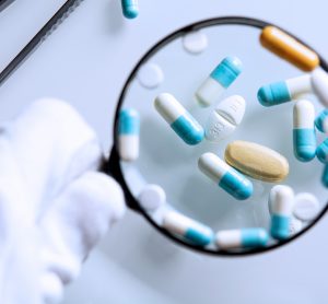 blue and white capsules and brown tablets under a magnifying glass - idea of QAQC or falsified medicines