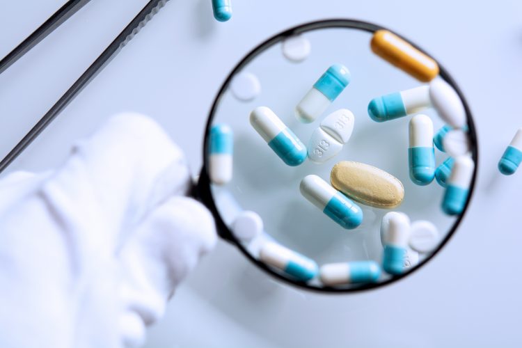 blue and white capsules and brown tablets under a magnifying glass - idea of QAQC or falsified medicines