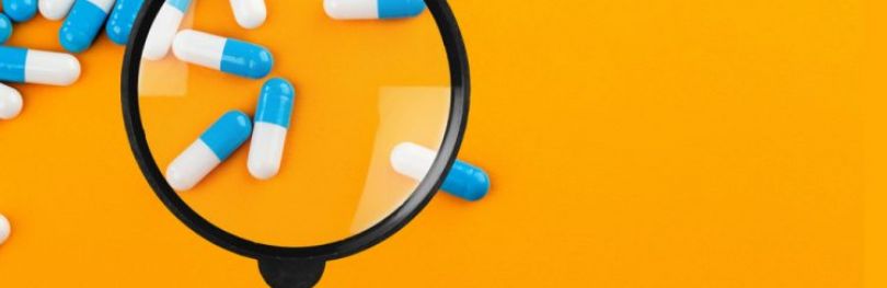 Blue and white capsules with magnifying glass over the top on bright orange background - idea of counterfeit identification or drug quality control