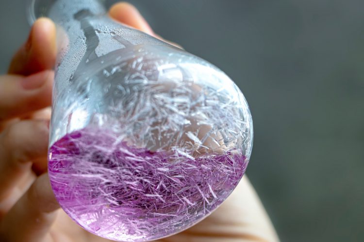 Thin, sharp and long white crystals in purple solution forming within a conical flask.