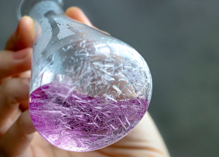 Thin, sharp and long white crystals in purple solution forming within a conical flask.