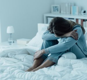 Woman sitting on bed with head on knees