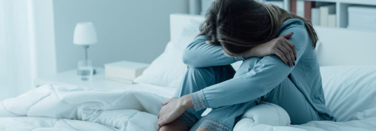 Woman sitting on bed with head on knees