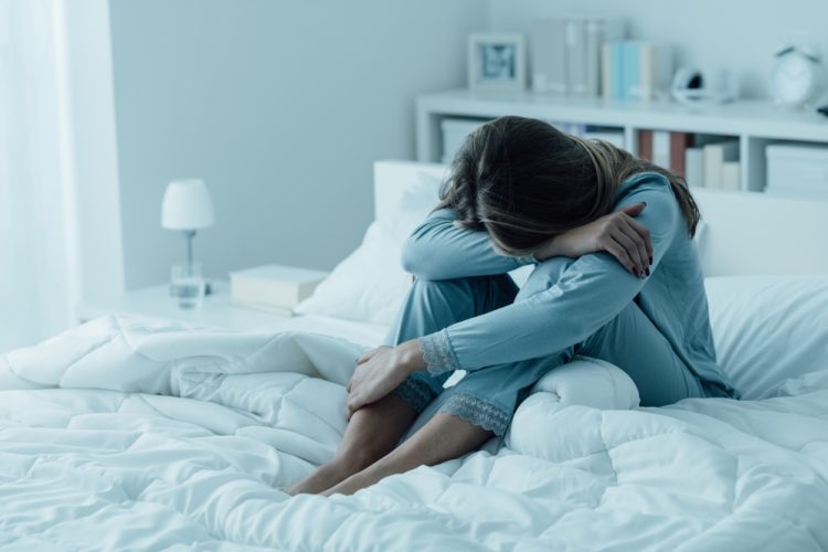 Woman sitting on bed with head on knees