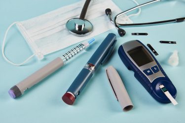 diabetes testing equipment and insulin pen next to face mask