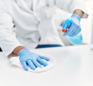 Cleanroom disinfection concept - close up of scientist wiping down a laboratory bench with a spray bottle of disinfectant and a white cloth