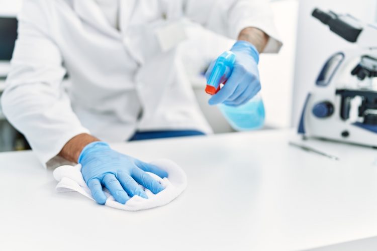 Cleanroom disinfection concept - close up of scientist wiping down a laboratory bench with a spray bottle of disinfectant and a white cloth