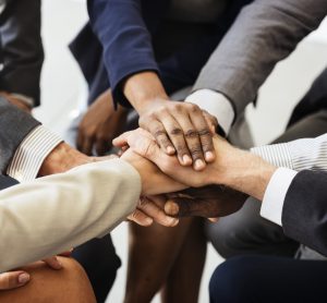 circle of people in suits with their hands together - diverse ethnicities and genders