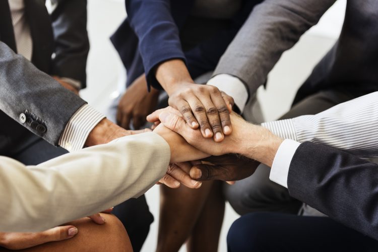 circle of people in suits with their hands together - diverse ethnicities and genders