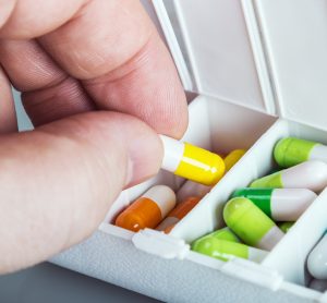 hand lifting yellow and white capsule from a sectioned drug box with other capsules of different colours in it