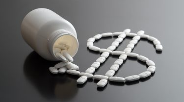 medicine bottle spilling white pills in the shape of a dollar sign - idea of pharma finances or drug pricing