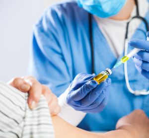 elderly woman recieving a vaccine from a doctor wearing blue srcubs, gloves and face mask