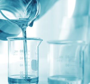 Pharmaceutical formulation development concept - person in white lab coat and gloves pouring a liquid from one beaker into another