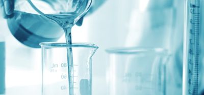 Pharmaceutical formulation development concept - person in white lab coat and gloves pouring a liquid from one beaker into another