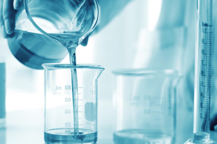 Pharmaceutical formulation development concept - person in white lab coat and gloves pouring a liquid from one beaker into another