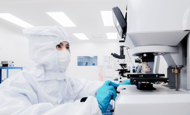 Gowned scientist using microscope