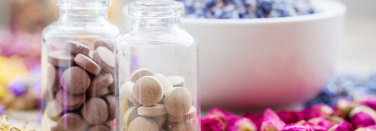 herbal medicine concept - glass bottles of brown pills surrounded by various herbs/petals