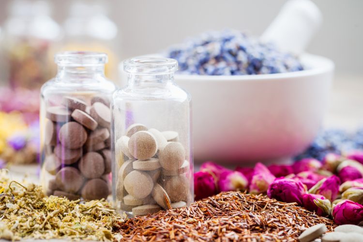 herbal medicine concept - glass bottles of brown pills surrounded by various herbs/petals