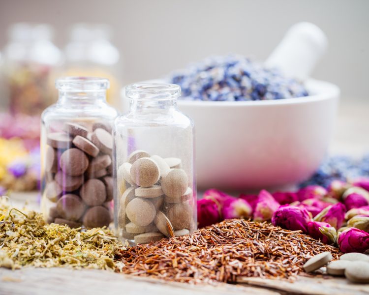 herbal medicine concept - glass bottles of brown pills surrounded by various herbs/petals